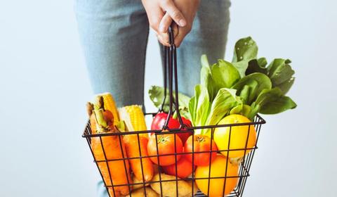 Jeune femme tenant un panier métallique chargé de fruits et de légumes