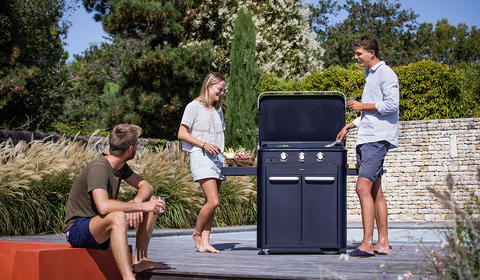 3 amis cuisinant sur une plancha installée sur la terrasse d'un jardin en plein été