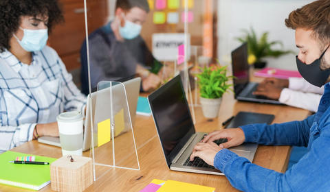 Collaborateurs et collaboratrices travaillant en openspace avec port du masque, à des bureaux aménagés pour répondre aux nouvelles normes sanitaires.