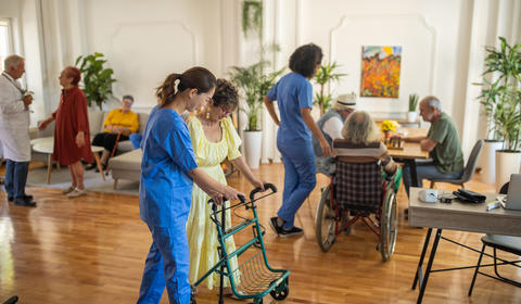 Une aide-soignante accompagnant un patient âgé se déplaçant avec une déambulateur.