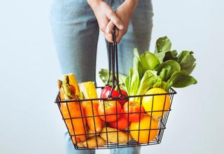 Jeune femme tenant un panier métallique chargé de fruits et de légumes