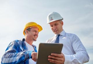 Un chef de chantier et un architecte discutant sur le terrain à l'aide d'une tablette