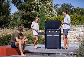 3 amis cuisinant sur une plancha installée sur la terrasse d'un jardin en plein été