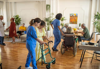 Une aide-soignante accompagnant un patient âgé se déplaçant avec une déambulateur.
