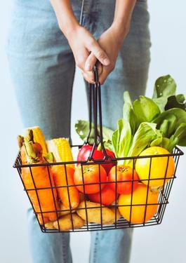 Jeune femme tenant un panier métallique chargé de fruits et de légumes