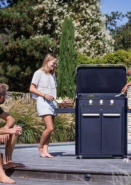 3 amis cuisinant sur une plancha installée sur la terrasse d'un jardin en plein été