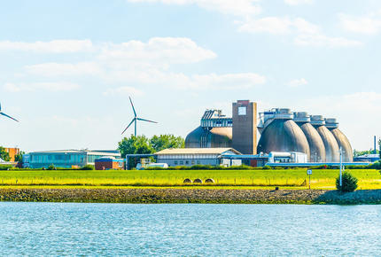 Vue extérieure d'une usine biomasse avec des éoliennes en arrière plan.