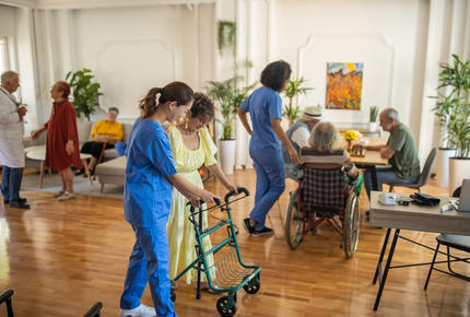 Une aide-soignante accompagnant un patient âgé se déplaçant avec une déambulateur.